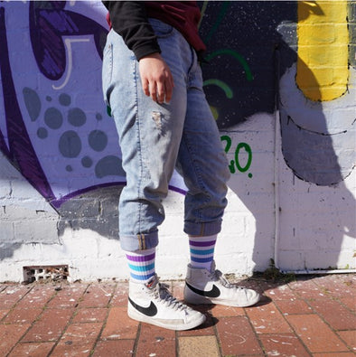 person wearing jeans and mid calf white socks with purple and blue striped socks