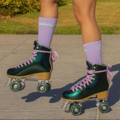 Person wearing green roller skates with purple laces on a sidewalk.
