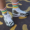 person wearing white mid calf socks with green, yellow and orange stripes and zebra shoes 
