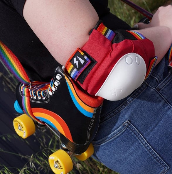 person wearing red elbow pad with rainbow strap holding rainbow roller skate