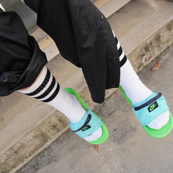 person wearing white mid calf socks with black sripes and slides 