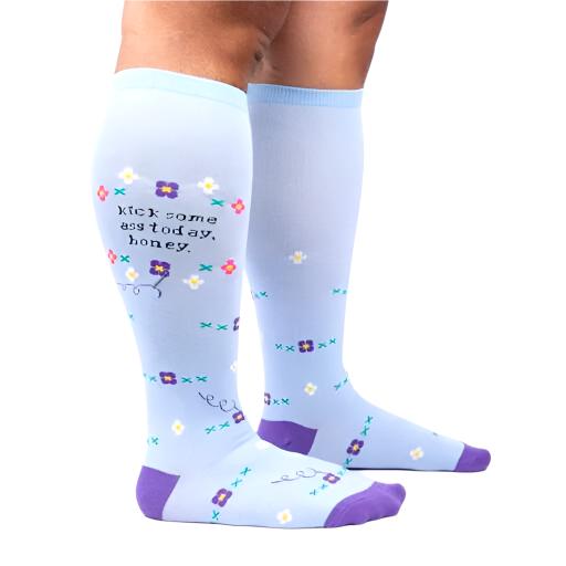 PERSON WEARING BABY BLUE KNEE HIGH SOCKS WITH PURPLE HEEL AND TOE AND PATTERN OF FLOWERS WITH TEXT "KICK SOME ASS TODAY. HONEY."