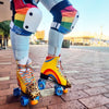 person wearing rainbow print striped knee pads, white caps  with yellow moxi roller skates 
