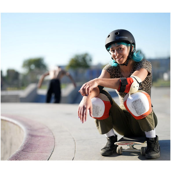 girl crouching down on skateboard wearing 187 killer padding orange creams and black knee pads elbow pads and wrist guards cream caps