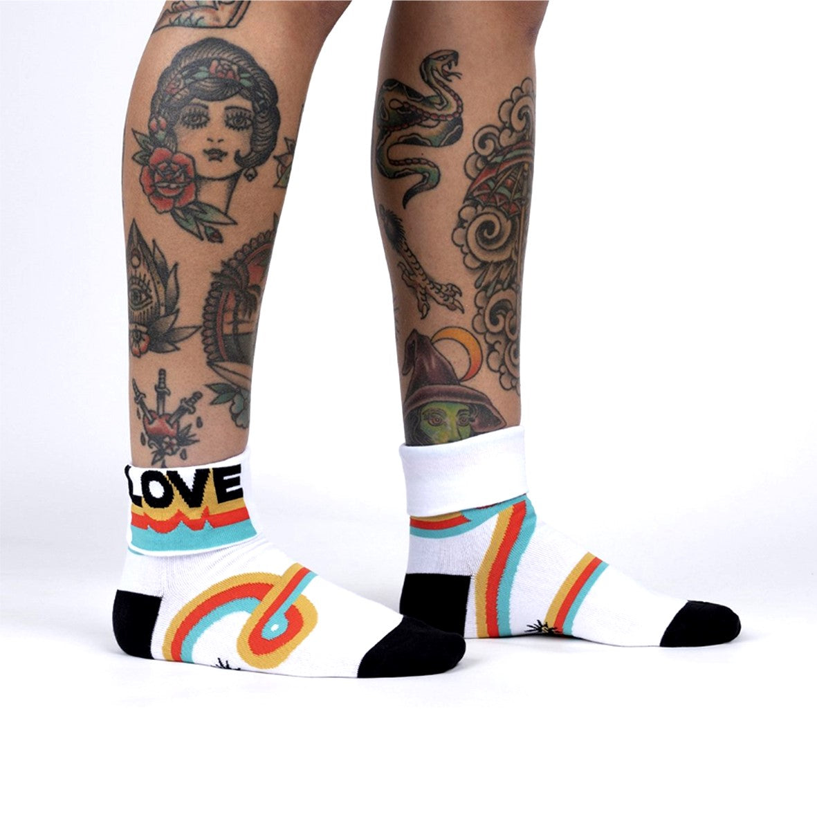 PERSON WEARING WHITE CREW SOCKWITH CUFF DOWN AND WORDS 'LOVE"  WITH BLACK HEEL AND TOE WITH PATTERN OF FUNKY STRIPES