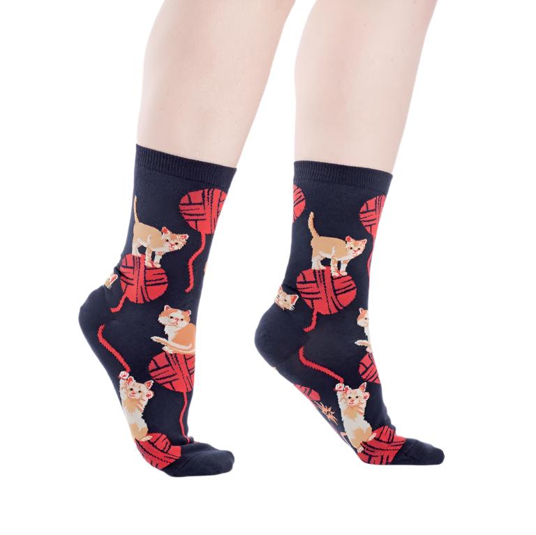 PERSON WEARING NAVY SOCKS WITH PATTERN OF ORANGE KITTENS STANDING ON RED BALLS OF WOOL