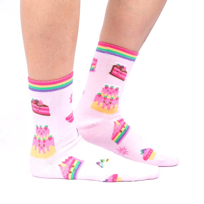 PERSON WEARING BABY PINK CREW SOCKS WITH PATTERN OF CAKES WITH CUTE FACES