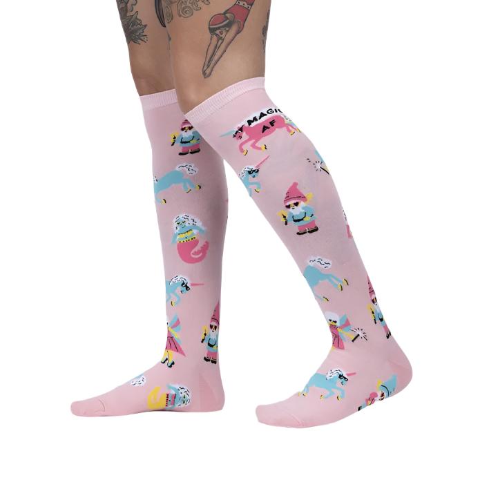 PERSON WEARING BABY PINK KNEE HIGH SOCKS WITH PATTERN OF UNICORNS FAIRYS AND GNOMES WITH GLASSES