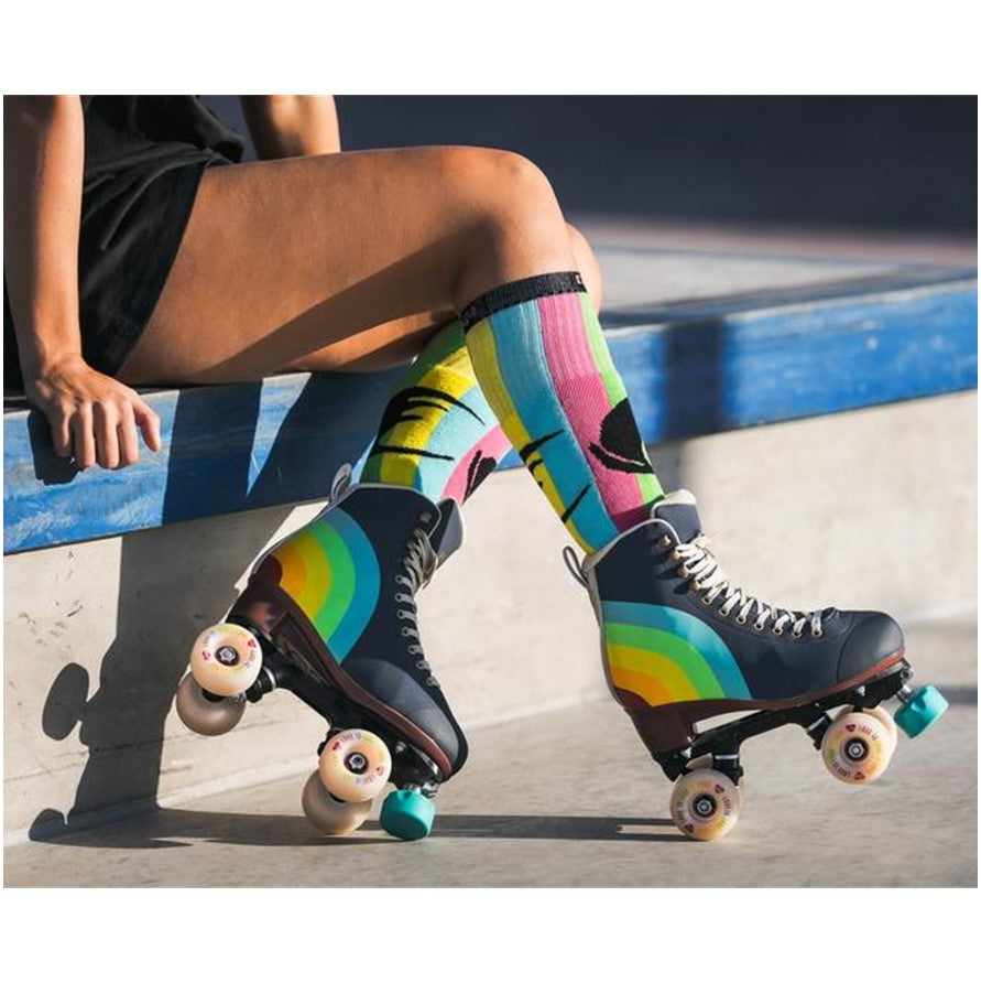 person wearing chaya navy blue rainbow retro roller skate, rainbow heel, white 'Love is love' outdoor wheels cream laces teal toe stops with rainbow socks