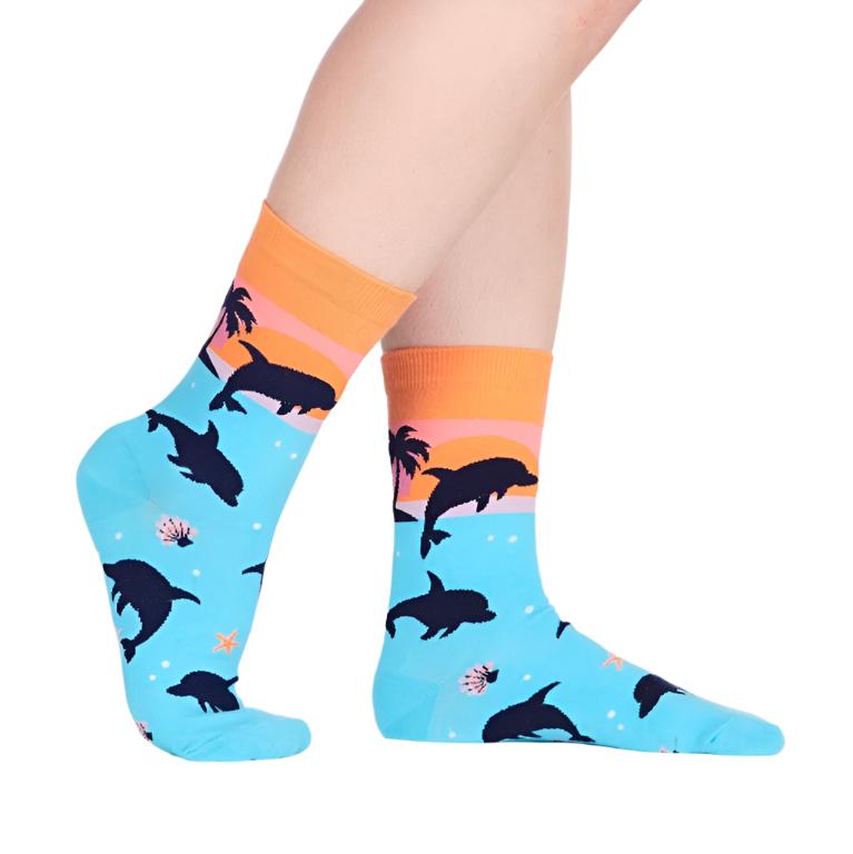 PERSON WEARING CREW SOCKS WITH PATTERN OF DOLPHINS JUMPING OUT OF WATER WITH SUNSET