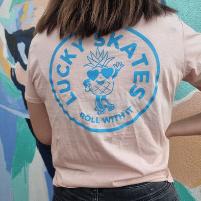 WOMENS WEARING PEACH TEE WITH BLUE LOGO OF PINEAPPLE WEARING ROLLER SKATES lucky skates roll with it 