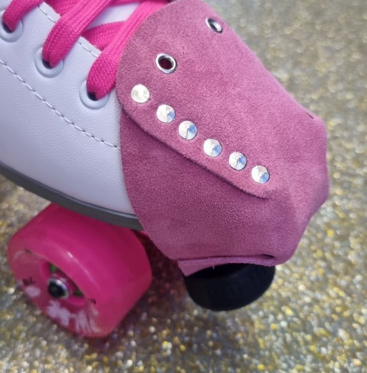 white rollerskate with pink wheels and light pink suede toe guard protectors with silver studs