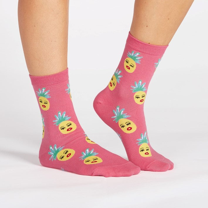 PERSON WEARING PINK CREW SOCKS WITH PATTERN OF PINEAPPLES WITH FACES